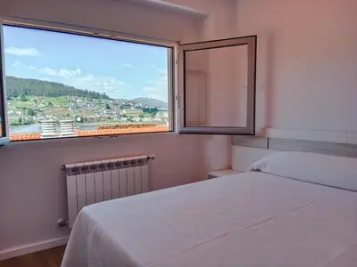 a bedroom with a bed and a large window at Atico en La Ría in Vivero