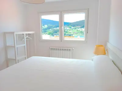 a white bedroom with a bed and a window at Atico en La Ría in Vivero