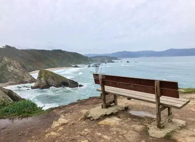 a bench sitting on the beach looking at the ocean at Apartamento Piscina 2G by Urraca Suites Viveiro in Viveiro