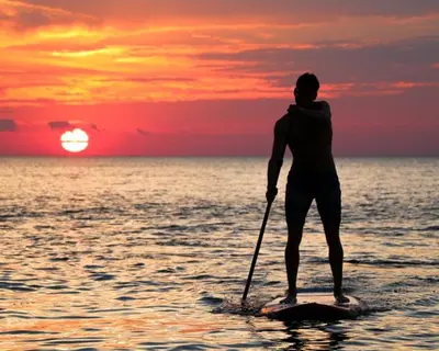 a man is standing on a paddle board in the ocean at Apartamento Piscina 2G by Urraca Suites Viveiro in Viveiro