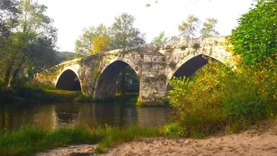 a stone bridge with two arches over a river at Casa A mi Vera in Covelo