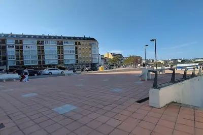 a parking lot with benches and a large building at Apartamento en Foz. Primera Línea Playa Rapadoira in Foz