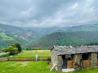 an old stone building in a field with mountains in the background at Casa Neto Goje in San Tirso de Abres