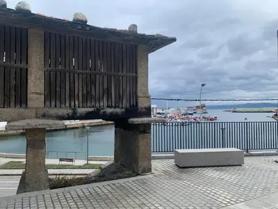 a building with a bench next to a body of water at Casita típica de pescadores -Casa Gloria- WIFI in Burela de Cabo