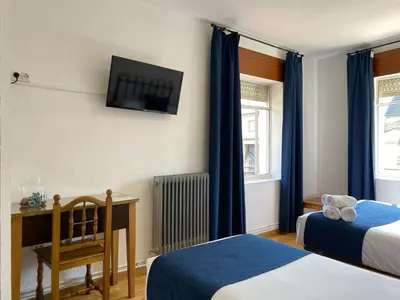 a bedroom with two beds and a television on the wall at Hostal La Trucha Sanabria in Puebla de Sanabria