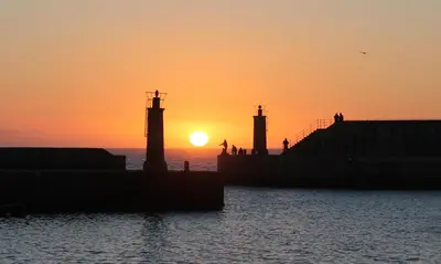 a sunset over the water with people walking on a pier at Hacienda El Esteiro - Villas vacacionales in Tapia de Casariego