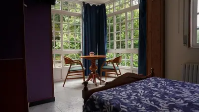 a bedroom with a table and chairs and windows at Pensión Castro Parrillada in Samos