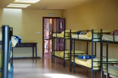 a room with four bunk beds in a room with a table at Albergue los Blasones in Sarria