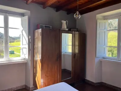 a bedroom with a wooden cabinet and two windows at Casa de Campo Pumarada de Oirín in Foz