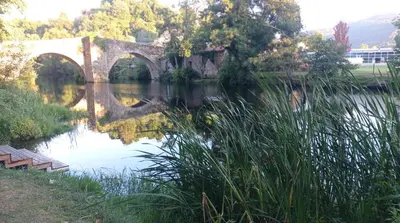 an old bridge over a river with trees in the background at PISO MANCE in Allariz