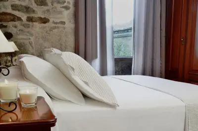 a bed with white pillows and a table with a candle at Sete Artes by Como en Casa in Santiago de Compostela