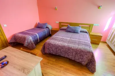 two beds in a room with pink walls and wooden floors at Hostal Rural La Tintoreria in Villablino