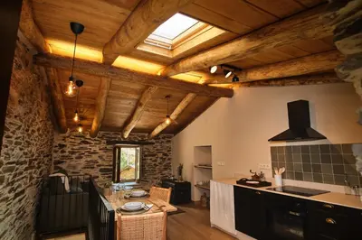 a kitchen with wooden ceilings and a stone wall at A Barreira -Lar da cima- in Folgoso