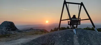 a person sitting in a swing on a rock with the sunset at Ás Portas do Sil - En la Ribeira Sacra in Villar de Cerreda