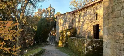 an old stone building with a clock tower in the background at Ás Portas do Sil - En la Ribeira Sacra in Villar de Cerreda