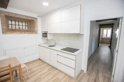 a kitchen with white cabinets and a wooden floor at Albergue A Fabrica in Santiago de Compostela