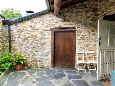 a stone house with a wooden door and chairs at Casa de las Flores / Casa de campo LUGO in A Pontenova