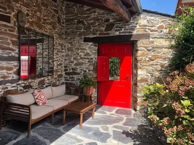 a red door and a couch in front of a building at Casa de las Flores / Casa de campo LUGO in A Pontenova