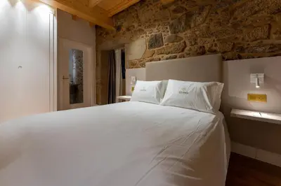 a bedroom with a white bed with a stone wall at Hostal HCELENIS in Caldas de Reis