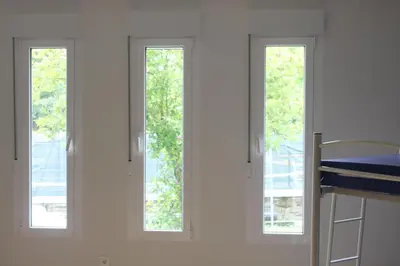 three windows in a white room with a bed at Pensión-Albergue Puente Ribeira in Sarria