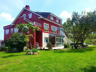 a large red house on a green lawn at Pensión Casa Elena in Reinante