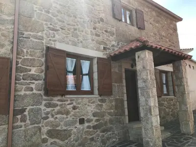a stone house with two windows with curtains in it at Villamia in Coirós