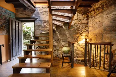 a room with a wooden staircase and a stone wall at Casa Muíñovedro in Chantada