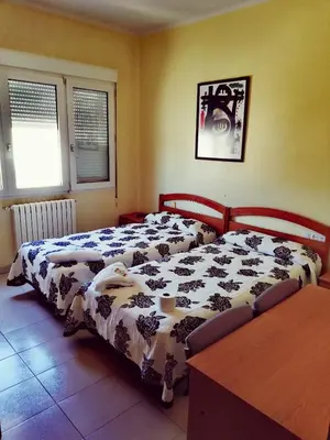 a bedroom with two beds and a table and two windows at Hostal Monteclaro in Ponferrada