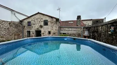 a large blue swimming pool in front of a building at Casa a Voada - Rural con Piscina Privada, Barbacoa y Juegos in Muiños