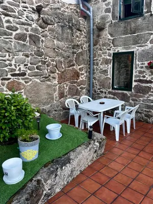 a patio with a table and chairs in front of a stone building at Casa a Voada - Rural con Piscina Privada, Barbacoa y Juegos in Muiños