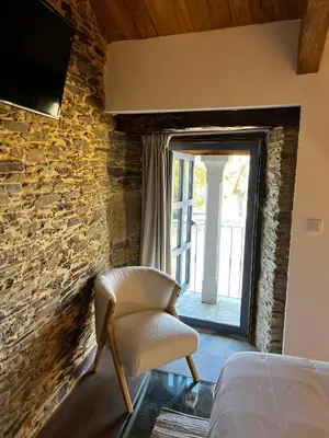 a bedroom with a chair in front of a stone wall at HOTEL CASAS DA FORTALEZA Casa da Torre in Outeiro de Rei