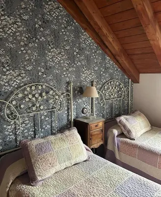 a bedroom with two beds and a wall with floral wallpaper at Casa Begoña in Igüeña