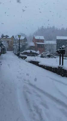 a snow covered street with cars and houses at Casa Begoña in Igüeña