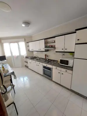 a kitchen with white cabinets and a white tile floor at Amplio Piso Reformado in Vivero