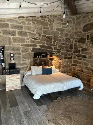 a bedroom with a bed in a stone wall at Aturuxo, Casa dos Mestres in Trasmiras