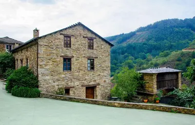 a large stone building with a mountain in the background at Casas Rurales Taramundi Verde in Taramundi