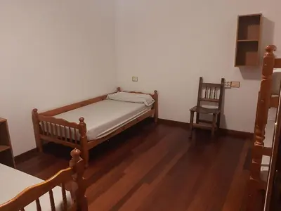 a small bedroom with a bed and a chair at Albergue Berce do Camiño in Tríacastela