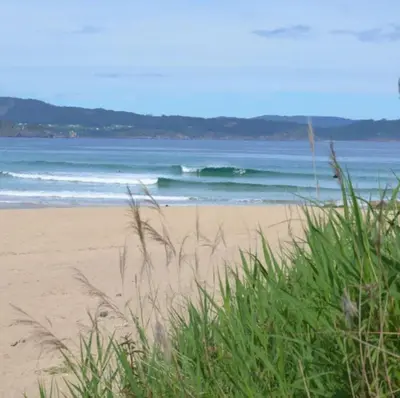 a beach with waves in the ocean and some grass at Los Castelos by Urraca Suites Viveiro in Viveiro