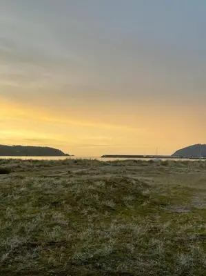 a field with the sun setting over the water at Appartement vistahermosa in Vivero