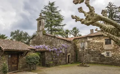 an old stone building with a church with purple flowers at Pazo de Andeade in Andeade