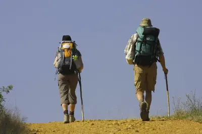 two people with backpacks walking on a dirt trail at Pensión Glorioso II in Picaraña