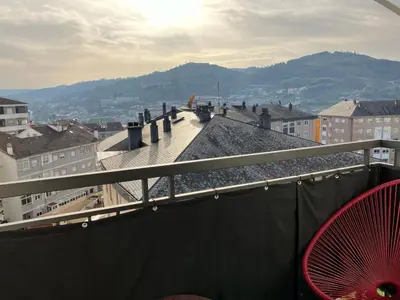 a red chair on a balcony with a view of a city at Vivienda estación in Ourense