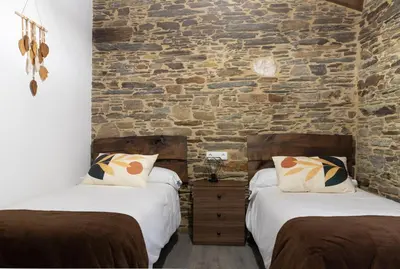 two beds in a room with a stone wall at Casa Rural Lar de Sanxes in A Pontenova
