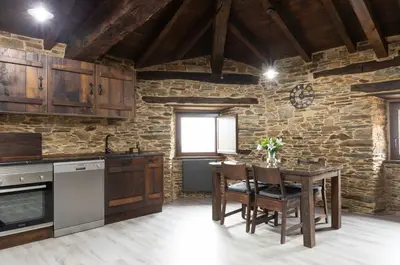 a kitchen with a table and a stone wall at Casa Rural Lar de Sanxes in A Pontenova