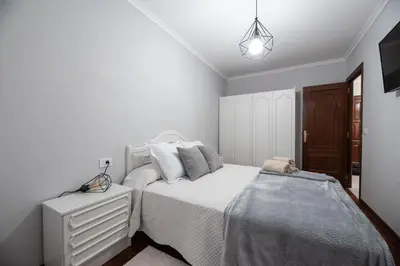 a white bedroom with a bed and a night stand at Apartamento acogedor centrico in Monforte de Lemos