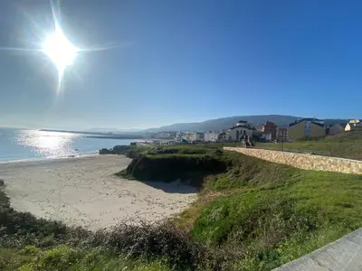 a sandy beach with the sun in the sky at Apartamentos LAMAROSA -LAS PLAYAS in Burela de Cabo