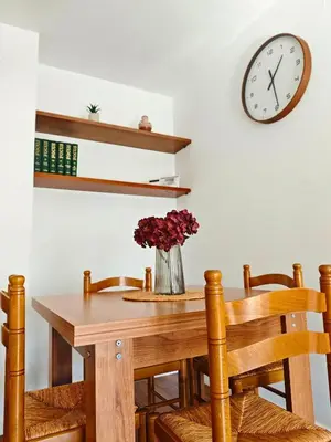 a dining room table with a vase of flowers and a clock at Apartamento Pena Furada in Ribadeo