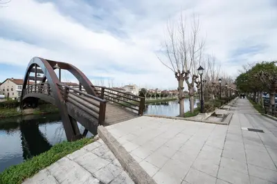 a wooden bench next to a river with a bridge at EREA apartamentos turísticos in Monforte de Lemos