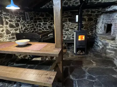 a wood burning stove in a stone room with a table at Ca Manín in Tineo