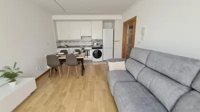 a living room with a gray couch and a kitchen at Piso Vega Foz in Foz